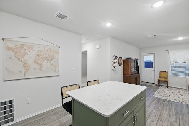 kitchen with green cabinetry, a kitchen island, light wood finished floors, and visible vents