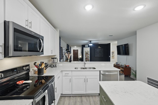 kitchen with white cabinets, appliances with stainless steel finishes, a sink, light countertops, and a peninsula