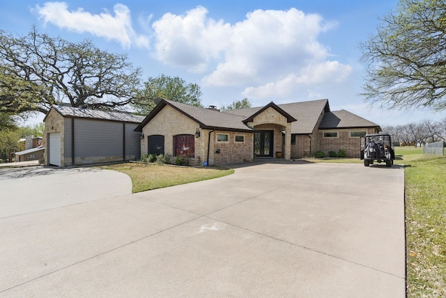 french country style house with brick siding, a front yard, driveway, and an outbuilding