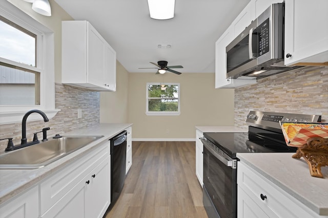 kitchen featuring ceiling fan, appliances with stainless steel finishes, a sink, light wood-style floors, and decorative backsplash