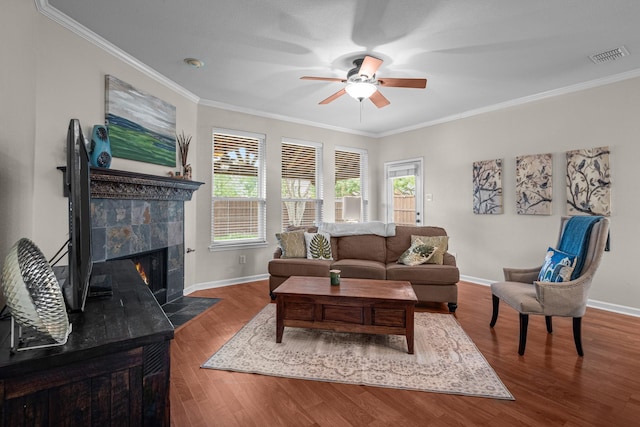 living room featuring wood finished floors, visible vents, ceiling fan, crown molding, and a tile fireplace