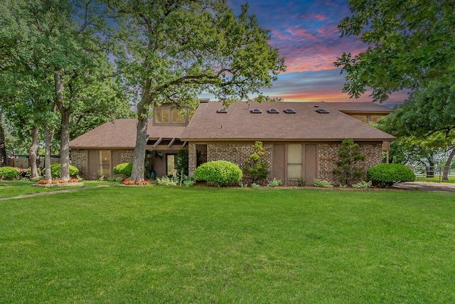 view of front of property with roof with shingles, brick siding, and a front yard