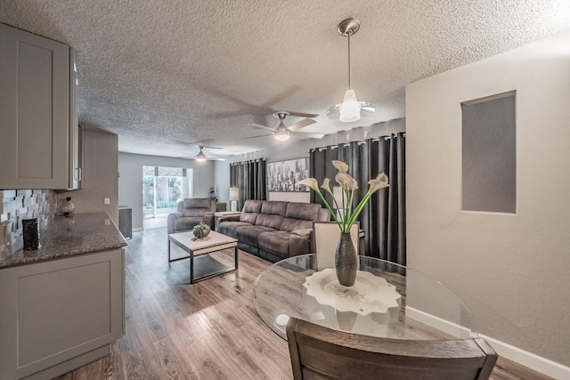 living room featuring baseboards, a textured ceiling, ceiling fan, and light wood finished floors