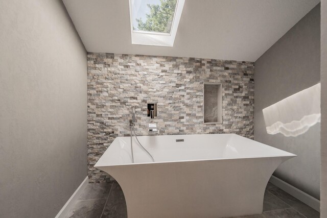 full bathroom with baseboards, a soaking tub, and lofted ceiling with skylight