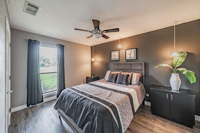 bedroom with visible vents, baseboards, a textured ceiling, and wood finished floors