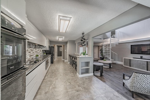 kitchen featuring a textured ceiling, tasteful backsplash, a sink, black appliances, and white cabinetry