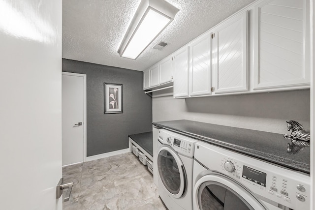washroom featuring a textured ceiling, visible vents, washing machine and dryer, cabinet space, and baseboards