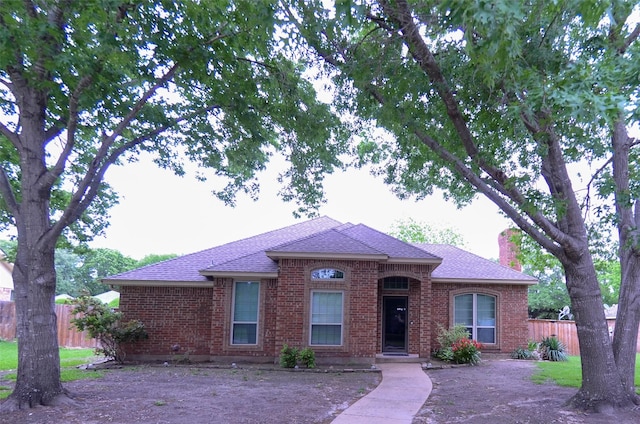 ranch-style home with brick siding, a shingled roof, fence, and a chimney