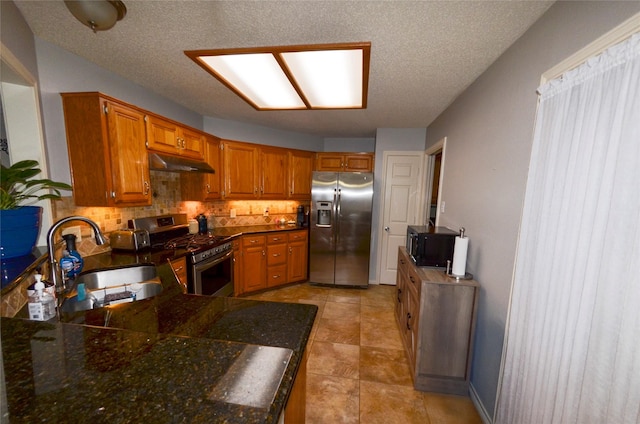 kitchen with appliances with stainless steel finishes, a sink, brown cabinetry, tasteful backsplash, and under cabinet range hood
