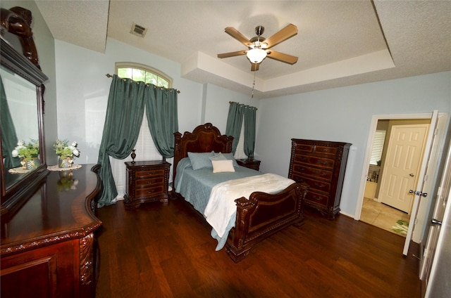 bedroom with visible vents, wood finished floors, baseboards, ceiling fan, and a tray ceiling