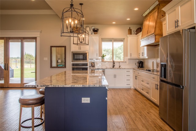 kitchen featuring white cabinets, appliances with stainless steel finishes, a sink, decorative backsplash, and a kitchen island