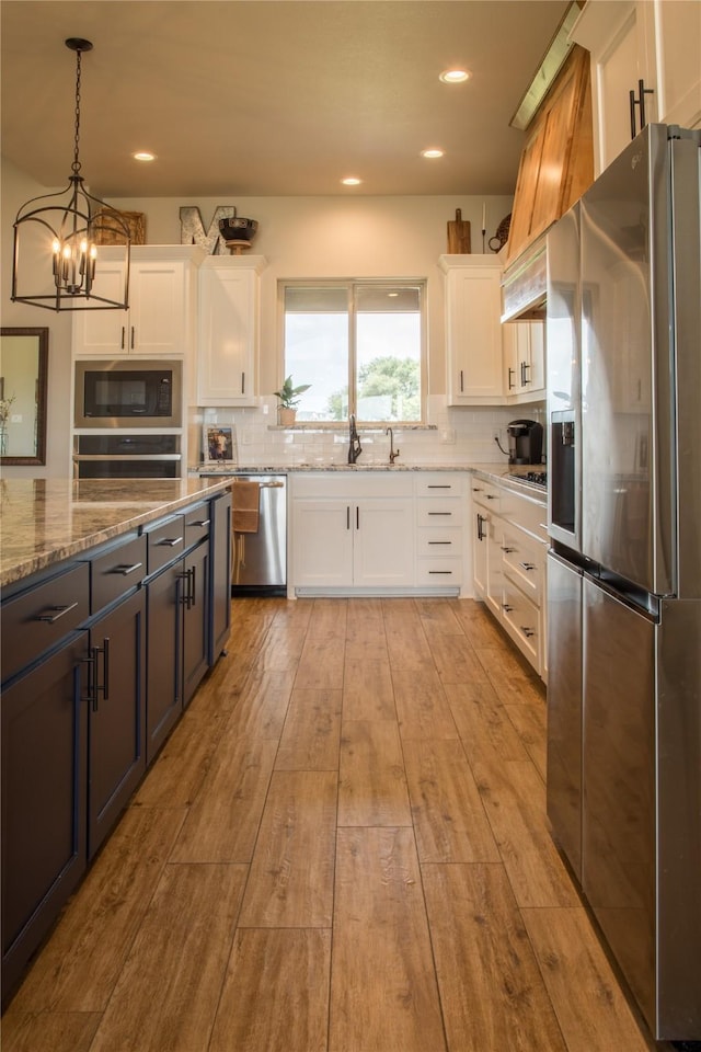 kitchen with tasteful backsplash, light stone counters, white cabinets, a chandelier, and stainless steel appliances