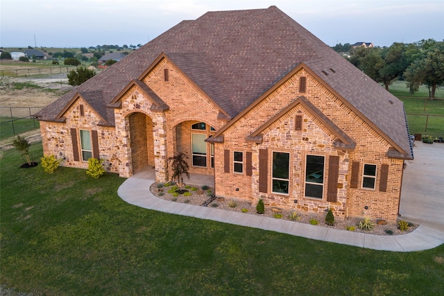 view of front facade with brick siding, a front lawn, roof with shingles, and fence