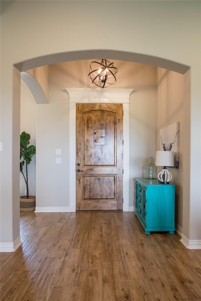entrance foyer featuring baseboards, arched walkways, and wood finished floors