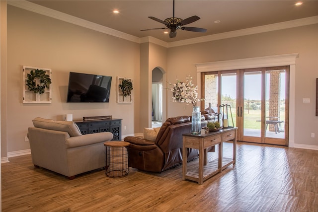 living area featuring crown molding, arched walkways, a ceiling fan, baseboards, and wood finished floors