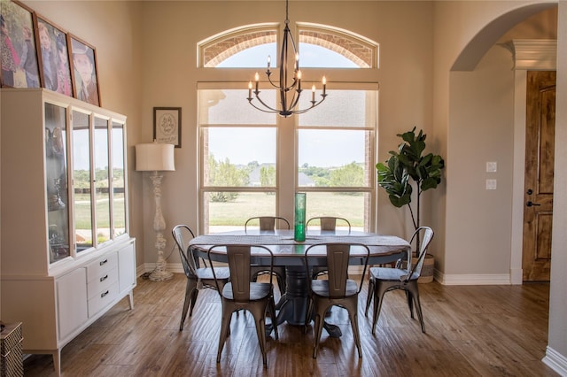 dining area with arched walkways, baseboards, a chandelier, and wood finished floors