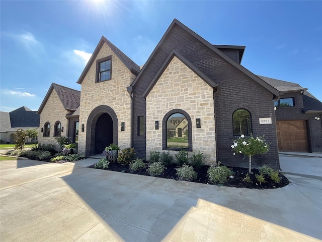 french country style house featuring driveway, brick siding, and stone siding