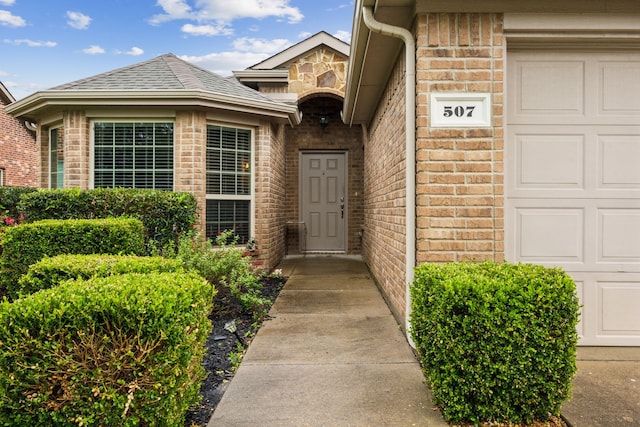 property entrance with a garage, a shingled roof, and brick siding