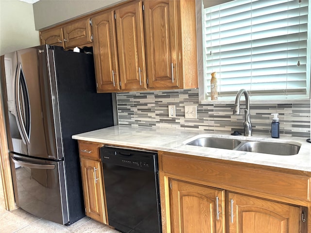 kitchen with decorative backsplash, brown cabinetry, dishwasher, a sink, and freestanding refrigerator