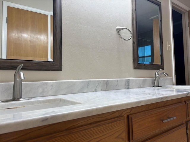bathroom featuring a sink, a textured wall, and double vanity