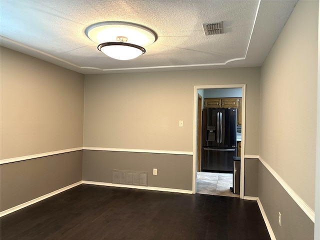 spare room featuring visible vents, a textured ceiling, baseboards, and wood finished floors