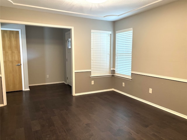 spare room featuring baseboards and dark wood finished floors
