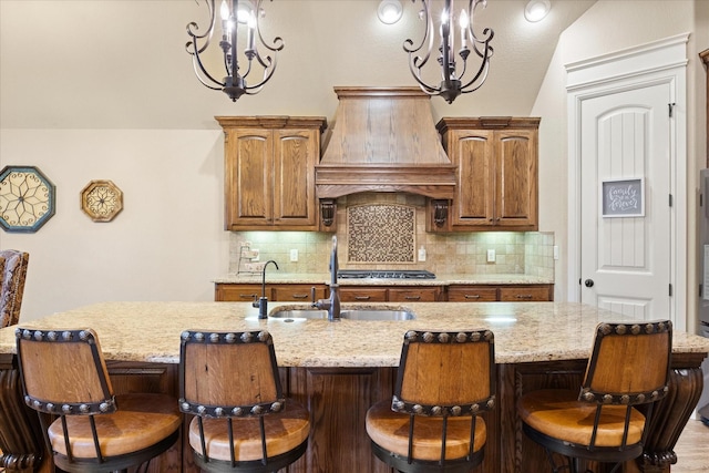 1408 Joshua Way, Granbury, TX 76048 - kitchen with a kitchen island with sink, backsplash, a sink, custom exhaust hood, and an inviting chandelier