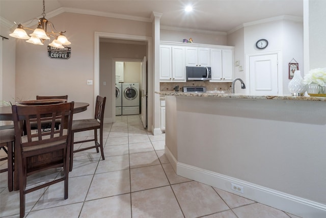 kitchen featuring light stone countertops, white cabinetry, stainless steel microwave, washing machine and clothes dryer, and range