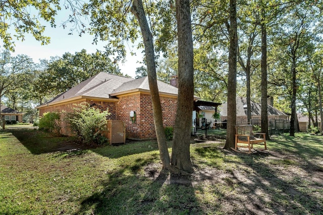 view of home's exterior with brick siding, a lawn, fence, and a chimney