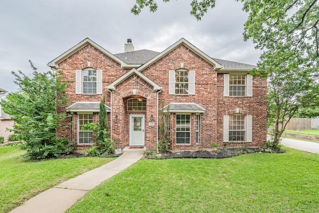 traditional-style home with brick siding, roof with shingles, a chimney, and a front yard