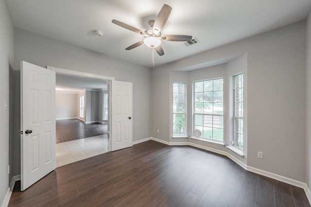 empty room with visible vents, dark wood finished floors, ceiling fan, and baseboards
