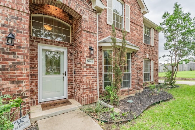 entrance to property with a lawn, brick siding, and fence