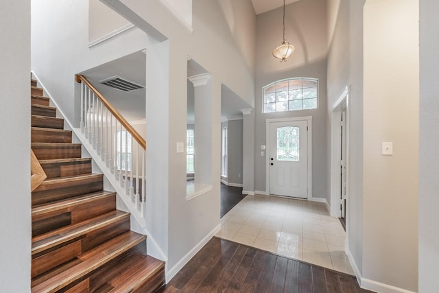 entrance foyer with visible vents, stairs, a towering ceiling, wood finished floors, and baseboards