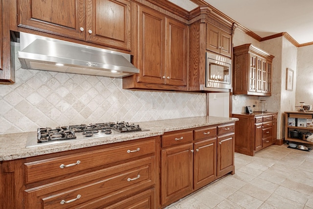 kitchen featuring brown cabinetry, ornamental molding, decorative backsplash, under cabinet range hood, and appliances with stainless steel finishes