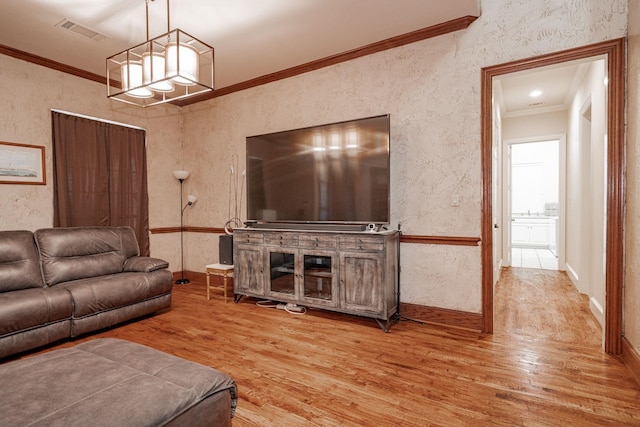 living area with visible vents, crown molding, wood finished floors, baseboards, and an inviting chandelier