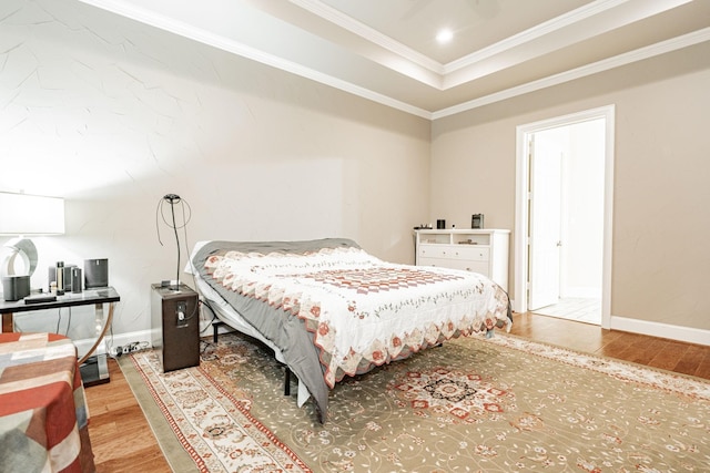 bedroom with baseboards, ornamental molding, a tray ceiling, and wood finished floors