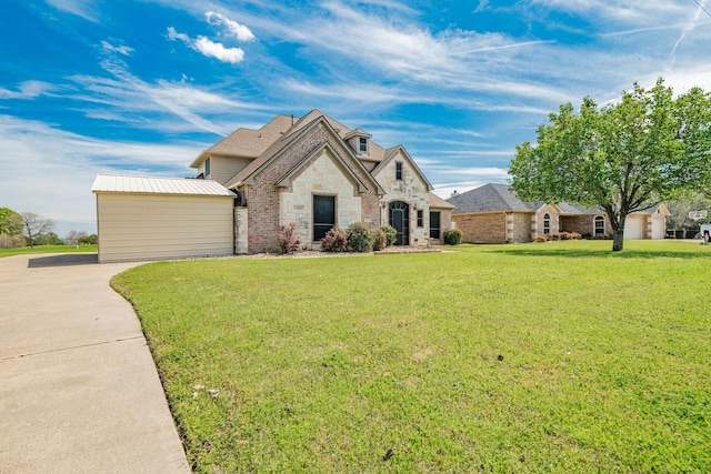 french provincial home with brick siding, stone siding, an outbuilding, and a front yard