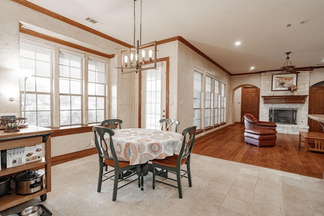 dining area with an inviting chandelier, a fireplace, arched walkways, visible vents, and ornamental molding