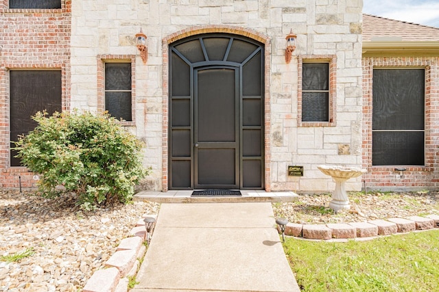 view of exterior entry featuring brick siding, roof with shingles, and stone siding