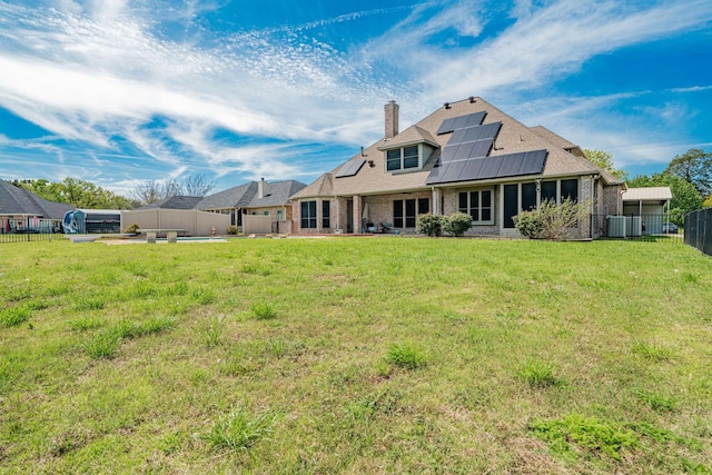 back of house featuring solar panels, a chimney, a lawn, brick siding, and a fenced backyard