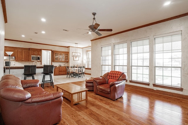 living area with crown molding, visible vents, plenty of natural light, and ceiling fan with notable chandelier