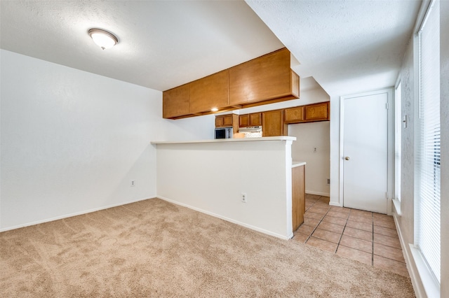 kitchen with light colored carpet, brown cabinets, a peninsula, stainless steel microwave, and baseboards