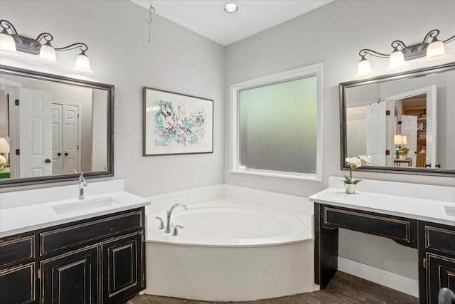 full bath with wood finished floors, a sink, a bath, and two vanities