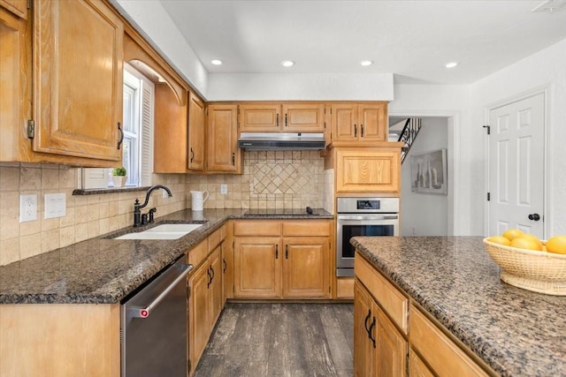 kitchen with appliances with stainless steel finishes, a sink, backsplash, under cabinet range hood, and dark wood-style floors
