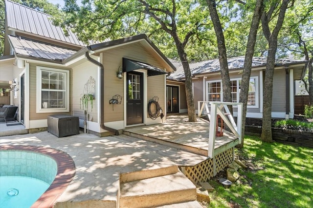 rear view of property with a deck, metal roof, and an outdoor pool