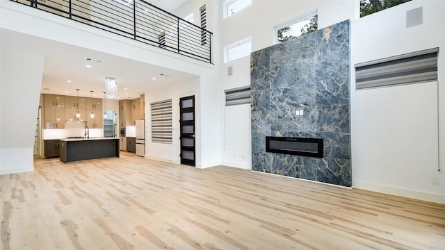 2316 Arroyo Ave, Dallas, TX 75219 - unfurnished living room featuring light wood finished floors, a high ceiling, a tiled fireplace, a sink, and baseboards