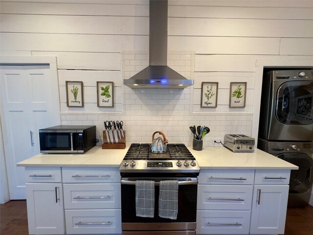 kitchen featuring gas stove, light countertops, stacked washer / drying machine, and wall chimney exhaust hood