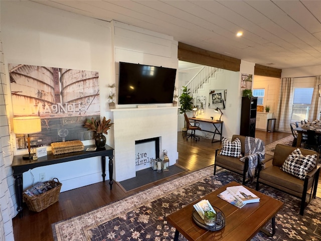 living room featuring a fireplace with flush hearth, stairs, and wood finished floors