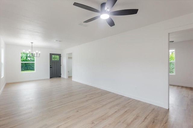 spare room with a wealth of natural light, ceiling fan with notable chandelier, light wood-type flooring, and visible vents