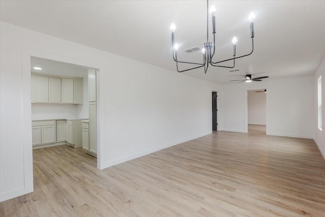 unfurnished dining area featuring baseboards, ceiling fan with notable chandelier, light wood-type flooring, and visible vents